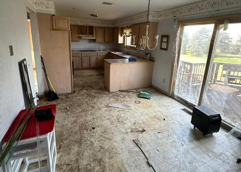 Estate kitchen and dining area before cleanout, showing clutter, debris, and old furniture.